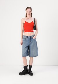 Haut court rouge avec bord blanc, short en jean bleu à mi-mollet et bottes noires à lacets, accessoirisé d'un petit sac noir.