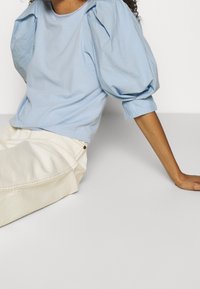 Top de manga corta azul claro con mangas abullonadas y voluminosas, hecho de tela suave. Combinado con pantalones de cintura alta en color blanco roto.
