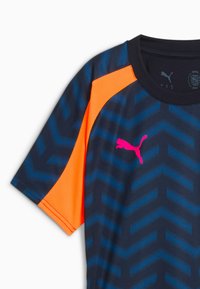 Puma urheilupaita, jossa on laivastonsininen pohja sinisillä sahalaitakuviolla, kirkkaan oranssit verkko-hihaiset ja vaaleanpunainen logo rinnassa.