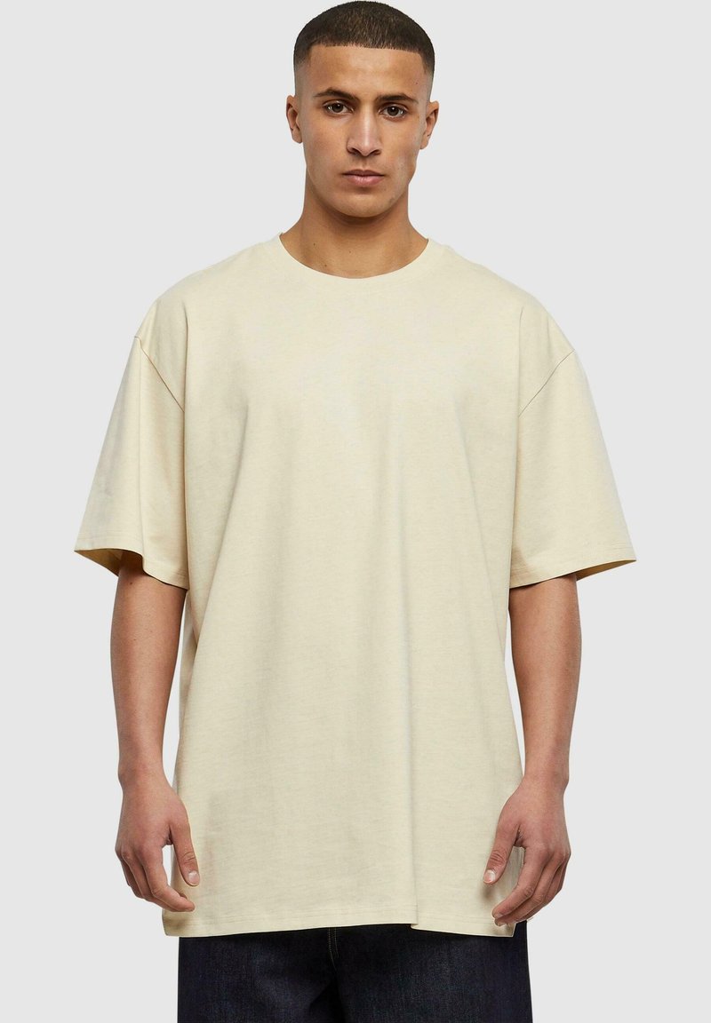 Tricou oversized bej din bumbac moale, cu mâneci scurte și guler rotund, asortat cu blugi din denim închis.
