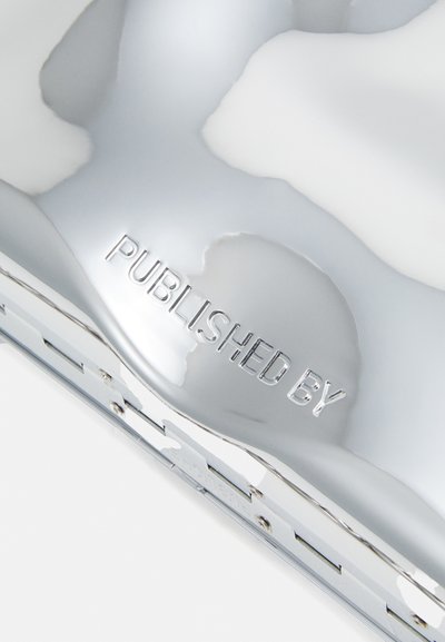 Metallic silver surface with a smooth, reflective finish. "PUBLISHED BY" is embossed, showing distinct letters. Minimalistic design.