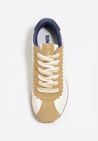 Zapatilla blanca y color arena con detalles de ante con forma de ola, cordones crema y un collar de textil azul marino. Presenta un logotipo beige en la lengüeta.