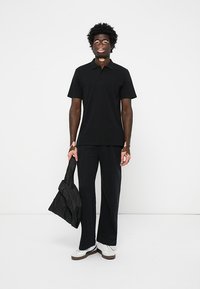 Fekete rövid ujjú poloing, fekete nadrág és egy könnyű fekete dzseki. A fehér sportcipők teszik teljessé az öltözetet.