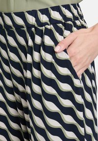 Pantalons fluides avec un motif ondulé en marine, blanc et vert olive. Taille élastique, poches latérales et texture de tissu lisse.