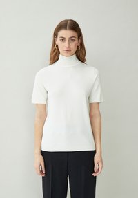Top de cuello alto de manga corta blanca en tejido suave y ligero. Presenta un cuello y dobladillo acanalados, con una silueta ajustada.