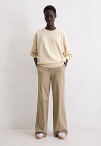 Crème sweatshirt met reliëftekst, gecombineerd met beige wijde broek en plateau schoen. Gladde stof met een relaxte pasvorm.