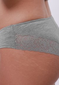 Prim-plan al șoldului unei persoane care poartă lenjerie gri cu dantelă, evidențiind textura naturală a pielii și vergeturile.