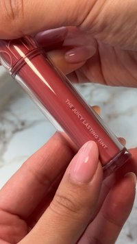 Lip tint i en transparent tub med en rosa-röd nyans. Har en smooth textur, cylindrisk form och präglat varumärke på sidan.