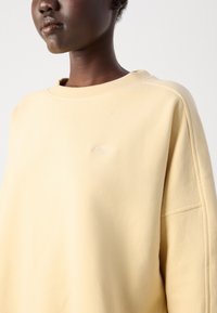 Ljusgul sweatshirt med avslappnad passform, rund hals och ribbade ärmslut. Har subtil broderi på bröstet och en jämn tygtextur.