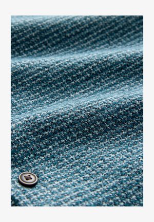 Primo piano di un tessuto blu texture con un piccolo bottone scuro cucito sul lato sinistro in basso.