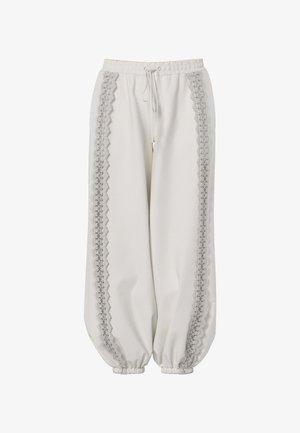 Pantalon blanc coupe ample avec poignets et taille élastiques, présentant une bordure en dentelle verticale le long des deux jambes et un cordon à l'avant.