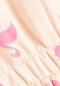 Ljusrosa tyg med ett mönster av rosa solar och musiknoter. Materialet verkar mjukt med en rynkad textur.