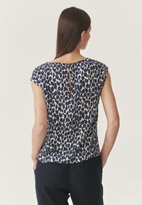 Tamsiai mėlynas ir grietinėlės spalvos bliusonukas su leopardų raštu, su švelniu rakto skylute nugaros dalyje ir laisvu kirpimu.