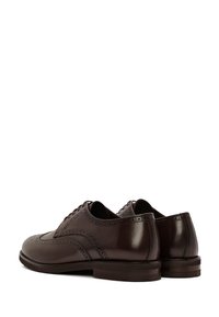 Chaussures de ville pour hommes en cuir brun foncé avec des détails en brogue, vues de dos et sur le côté sur un fond blanc.