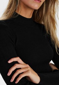 Črni rebrast turtleneck pulover z dolgimi rokavi, ki ima prilegajočo se zasnovo in gladko teksturo, razkriva dekolte in del rokavov.