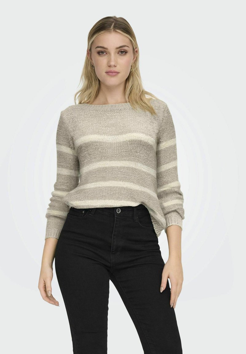 Pull en tricot beige avec des rayures horizontales crème, col rond et poignets côtelés, associé à un jean noir taille haute.