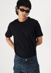 Black short-sleeve t-shirt made from smooth fabric, paired with blue denim cargo pants featuring multiple pockets and a zipper detail.