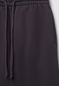 Pantalons de survêtement violet foncé en tissu doux, avec une taille élastique et un cordon de serrage, et une texture lisse.