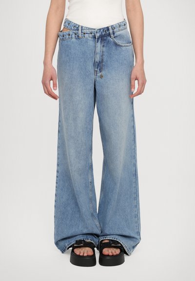 Jean en denim bleu clair à jambe large, taille haute, grandes poches et boutons décoratifs. Tissu texturé avec un ourlet brut.