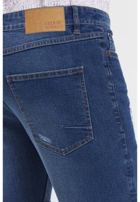 Mörkblå jeans i denim med en lätt sliten textur, med en brun läderflik vid midjan och vanliga bakfickor.