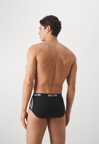 Sorte atletiske svømmedragter med en tætsiddende pasform, der har en kontrasterende hvid talje med logo og tre hvide striber på siderne.