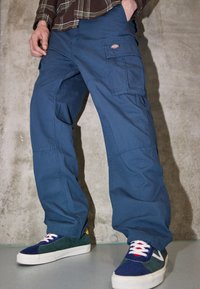 Blå cargobyxor gjorda av tålig material med fickor på sidorna. Bar med flerfärgade sneakers som har en vit sula och snörning.