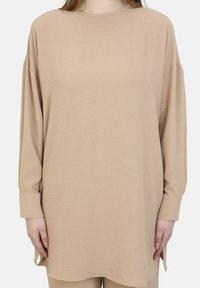 Maglia beige a maniche lunghe con tessuto testurizzato, scollatura rotonda e vestibilità comoda. Presenta spacchi laterali all'orlo e maniche con polsini.