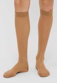 Meias até ao joelho de cor castanho-claro com uma textura suave, faixa superior elástica e design de ponta aberta, adequadas para vários tamanhos de pé.