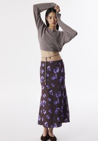 Hnědý pletený crop top s dlouhými rukávy, spárovaný s maxi sukní s fialovým květinovým vzorem, která má ve své pase dekorativní opasek.