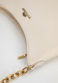 Borsa a tracolla in pelle beige con superficie texture, accessori in oro e tracolla a catena. Presenta una chiusura con zip e un logo in evidenza.