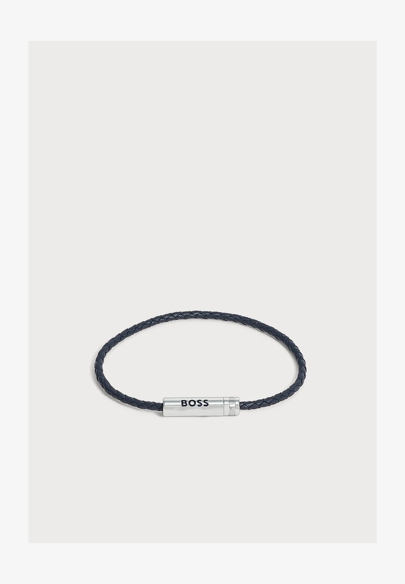 Bracelet en cuir tressé noir avec fermoir cylindrique en argent gravé du mot "BOSS" sur fond blanc.