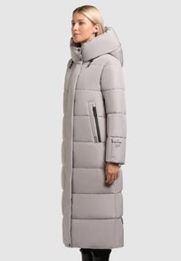 Cappotto lungo trapuntato in grigio chiaro, con colletto alto, tasche con zip e dettaglio del logo sulla manica. Materiale liscio e resistente all'acqua.