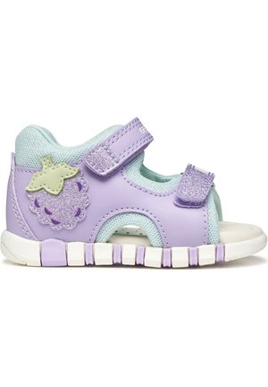 Sandale violette pour tout-petit avec des brides en Velcro, une doublure en mesh bleu clair, une semelle blanche flexible, et un patch pailleté en forme de raisin sur le côté.