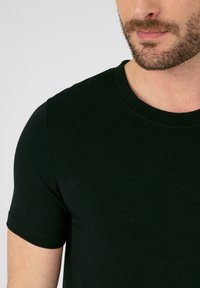 Camiseta negra de manga corta hecha de una tela suave, con un escote redondo y un diseño ajustado, con detalles de textura visibles.