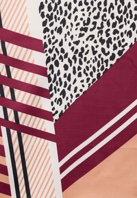 Αφηρημένο γεωμετρικό μοτίβο με μπορντό ρίγες, μαύρες βούλες με σχέδιο ζώου, ροδακινί διαγώνιες γραμμές και συμπαγείς ροδακινί και μπορντό μορφές.