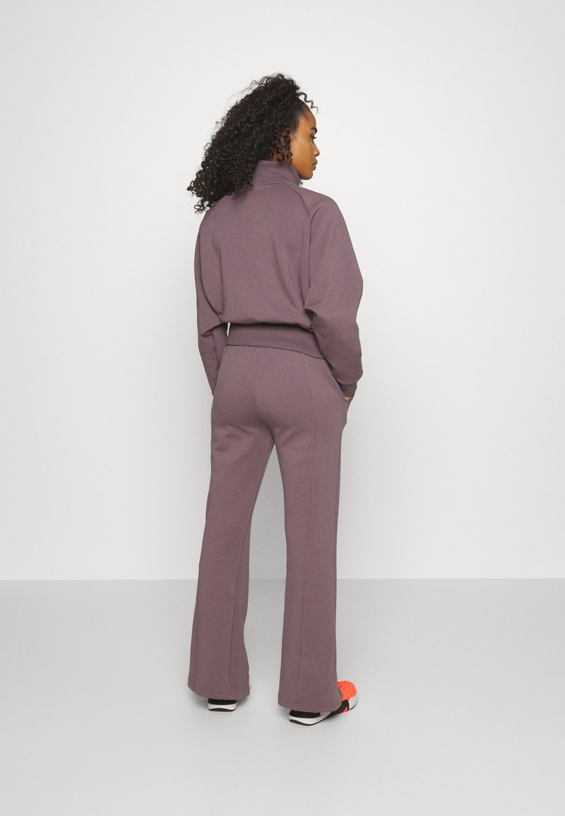 Lila Sweatshirt und passende ausgestellte Hose aus weichem Material, mit hohem Kragen und Akzentdetails an den Ärmelbündchen und am Saum.