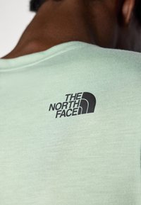 Camiseta de manga corta verde claro hecha de tela suave, con un logo negro de "The North Face" en el hombro izquierdo.