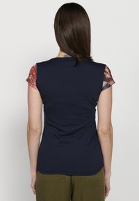 Camiseta ajustada de color azul marino con mangas cortas de patrón en rojo y azul. Textura suave con cuello redondo y silueta entallada.