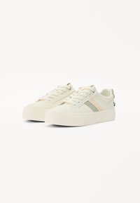 Zapatillas de lona blancas con acentos en verde claro y melocotón, puntera redonda, suela gruesa, diseño con cordones y detalle del logo en el talón.