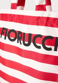 Närbild av en röd och vit randig tygv�äska med svart "FIORUCCI"-text och sydda handtag.