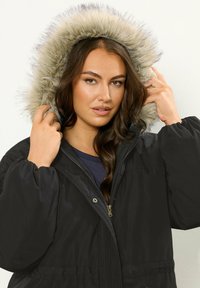 Mustat puffatakit, joissa on tekoturkista vuorattu huppu, vetoketjullinen etuosa, joustavat hihansuut ja väljä istuvuus, joka tarjoaa sileän ulkopintarakenteen.