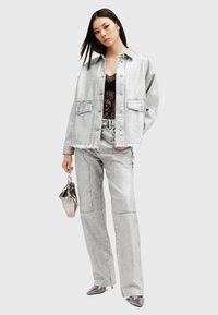Conjunto de chaqueta y pantalones de mezclilla gris claro, con un acabado desgastado, camiseta de encaje debajo y un pequeño bolso plateado.