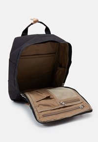 Mochila preta com pega superior, totalmente aberta para revelar um interior castanho com bolso com fecho e bolsos em rede dentro do flap frontal.