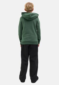 Sweatshirt vert avec une poche kangourou et une capuche, associé à un pantalon noir ample. Vue arrière, avec une texture lisse et sans motifs visibles.