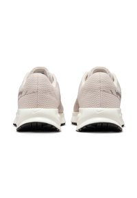 Un paio di scarpe da running Nike beige viste di lato, con tomaia in tessuto testurizzato e suole intermedie bianche con suole esterne nere.