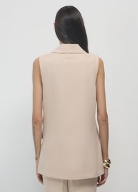 Gilet beige senza maniche con colletto a risvolto e texture liscia, caratterizzato da un taglio sartoriale e un design pulito e minimalista.