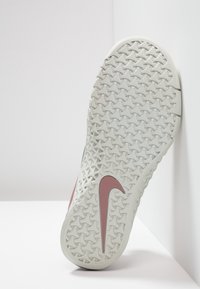 Suela de sneaker de goma gris claro con un patrón de diamantes texturizado y un logo de swoosh de Nike en color rosa. El diseño es deportivo y contemporáneo.
