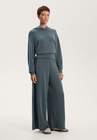 Set di comode loungewear in teal, leggero, composto da una felpa oversize con tasca a marsupio e pantaloni a gamba larga dalla trama morbida.