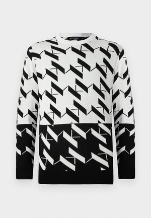 Black and white long-sleeve sweater with bold geometrical zigzag and diagonal line pattern, round neckline, and ribbed cuffs and hem.