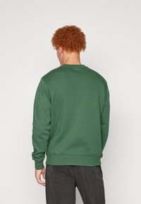 Grön sweatshirt med rund halsringning och ribbade ärmslut, tillverkad av en mjuk bomullsblandning. Har en minimalistisk design utan synliga logotyper.